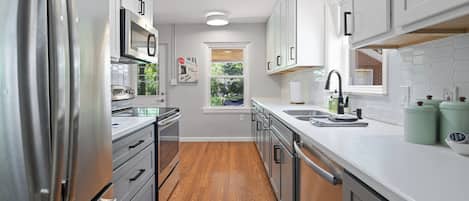 Una cocina moderna con electrodomésticos de acero inoxidable, armarios blancos y piso de madera.