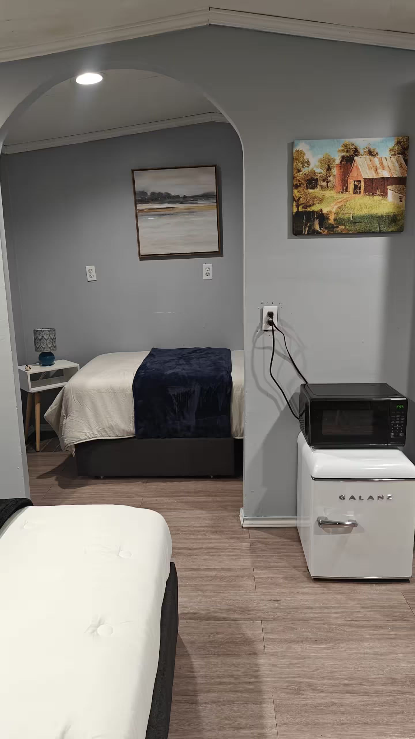 Un dormitorio con una cama, una mesita de noche, un cuadro en la pared y un microondas.