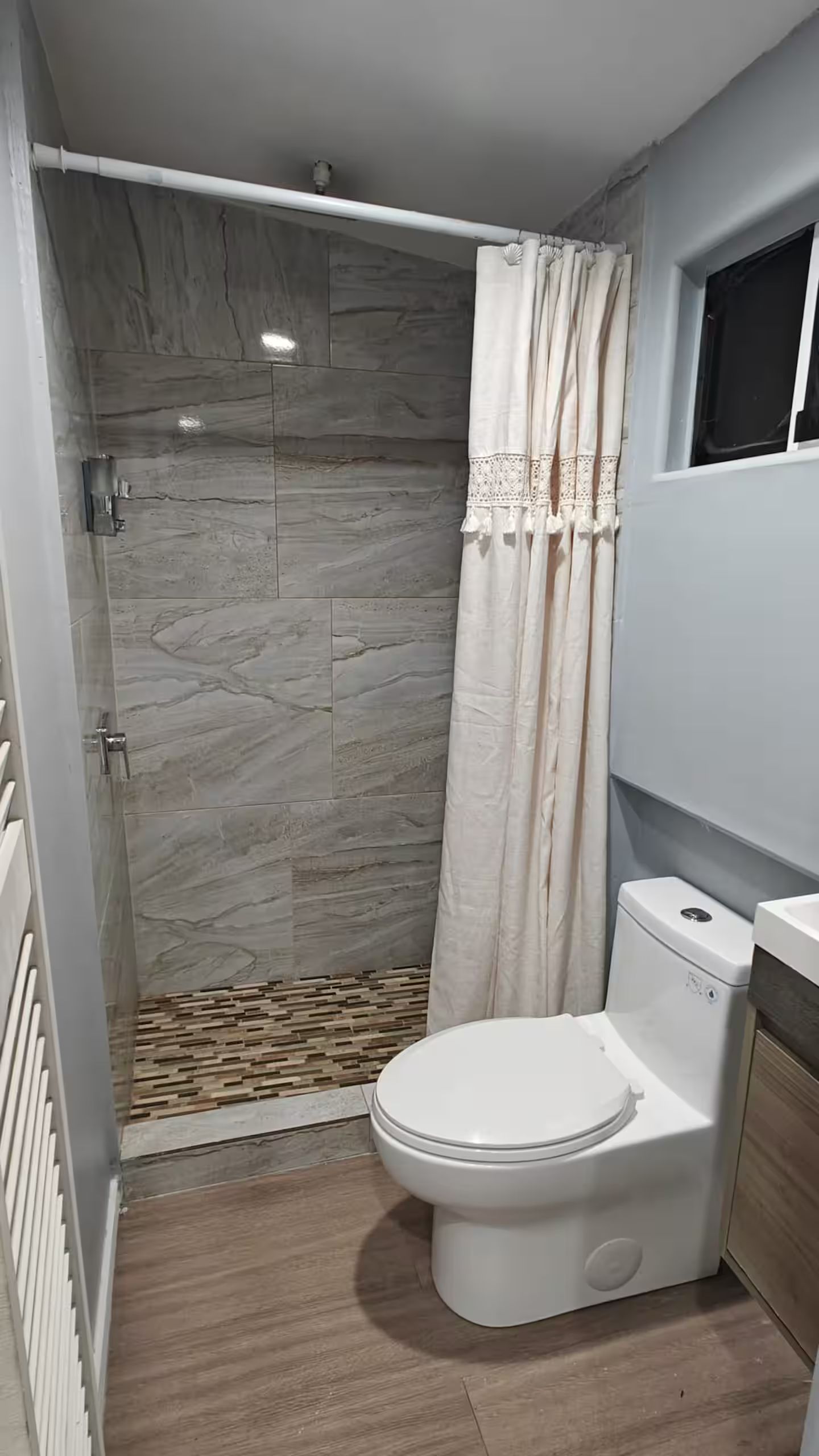 Un baño con ducha, inodoro y ventana.