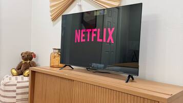 Un téléviseur posé sur un meuble en bois, avec un ventilateur fixé au mur juste au-dessus.