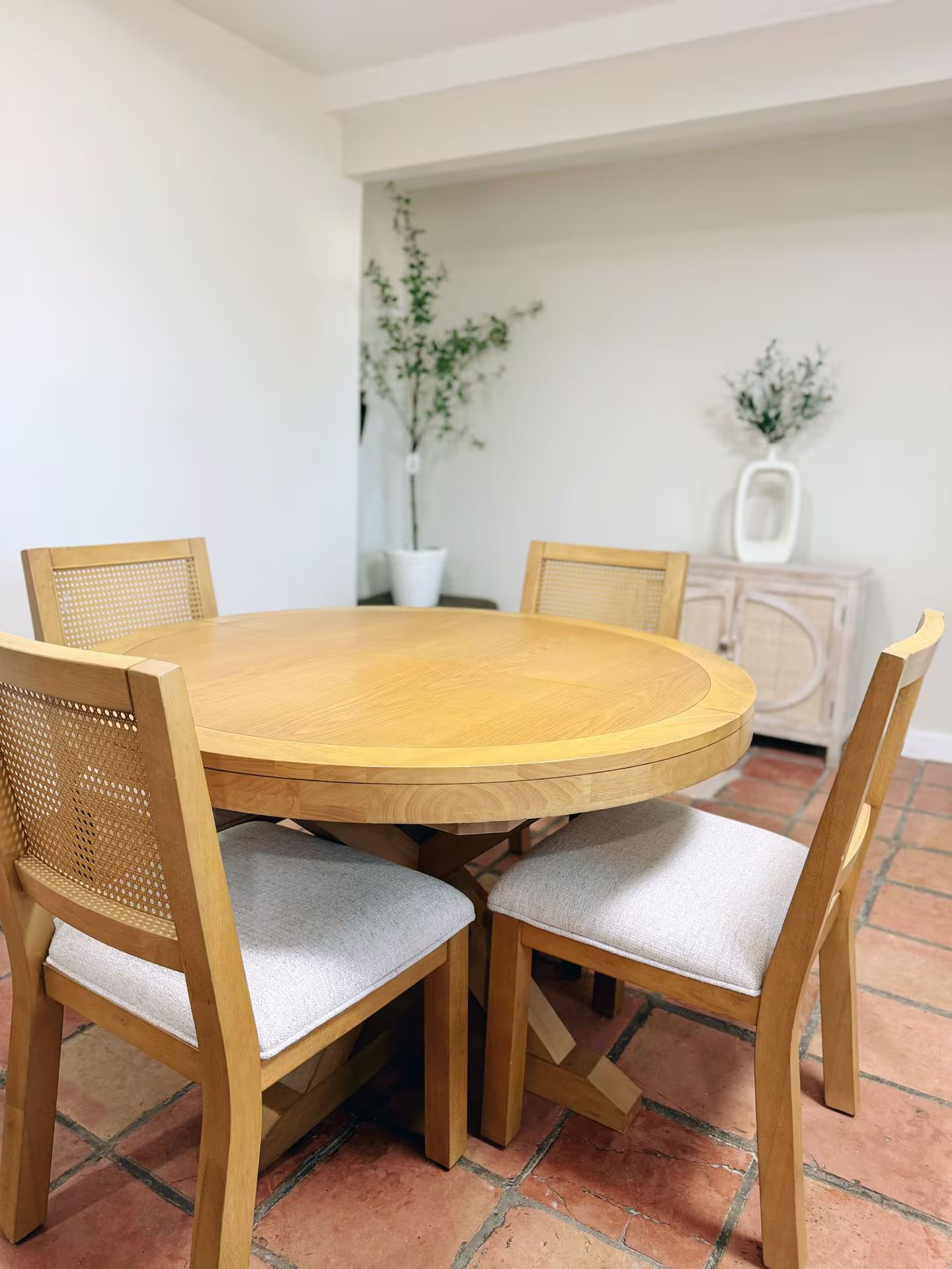Une table de salle à manger ronde en bois, accompagnée de quatre chaises, chacune dotée d’un dossier en osier et d’un siège rembourré.