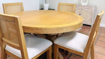 Une table de salle à manger ronde en bois, accompagnée de quatre chaises, chacune dotée d’un dossier en osier et d’un siège rembourré.