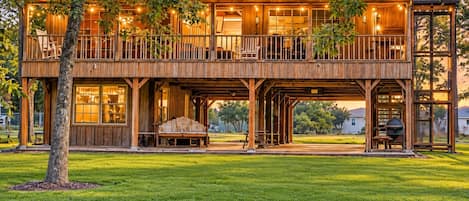 A two-story wooden cabin with a balcony, outdoor seating, and a barbecue area.