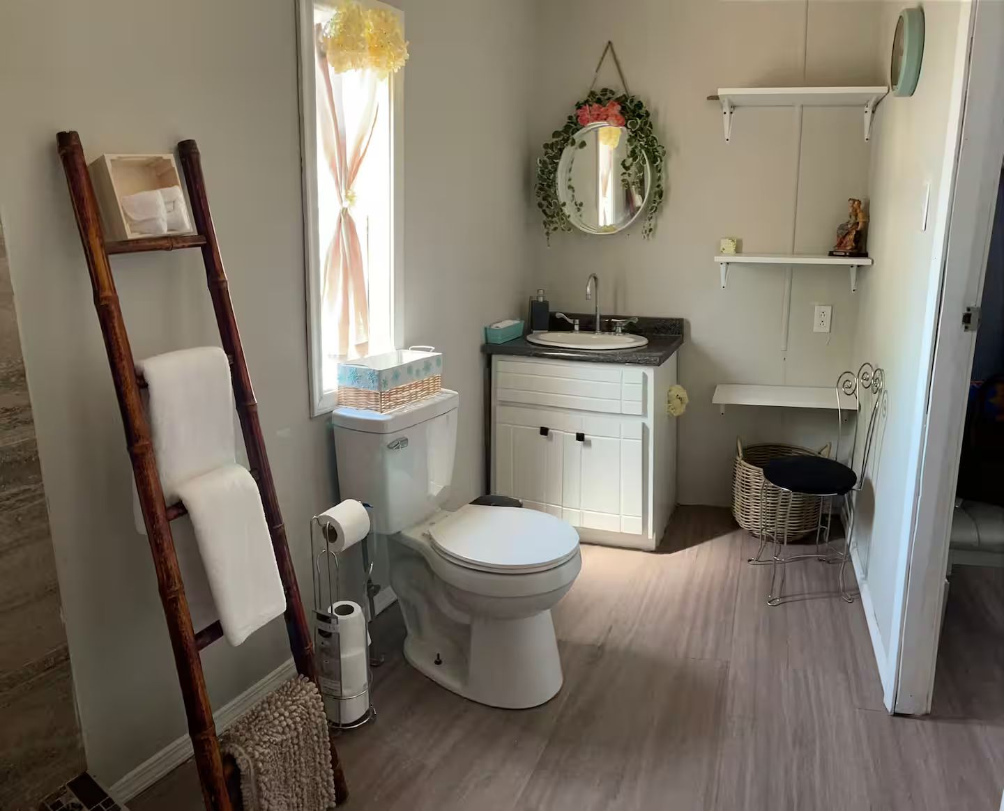 Un baño con inodoro, lavamanos y espejo. Se ve una escalera de madera, una cesta y una silla de mimbre.