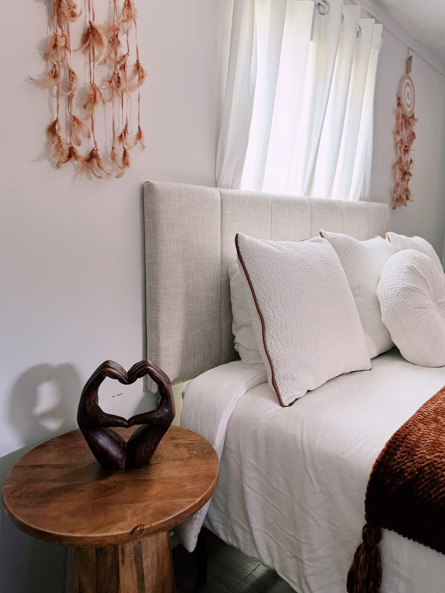 A bedroom with a bed, pillows, a wooden nightstand, and a decorative heart-shaped object.
