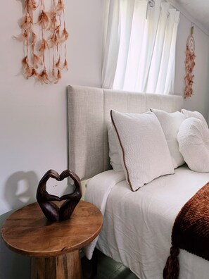 Une chambre à coucher avec un lit, des oreillers, une table de chevet en bois et un objet décoratif en forme de cœur.