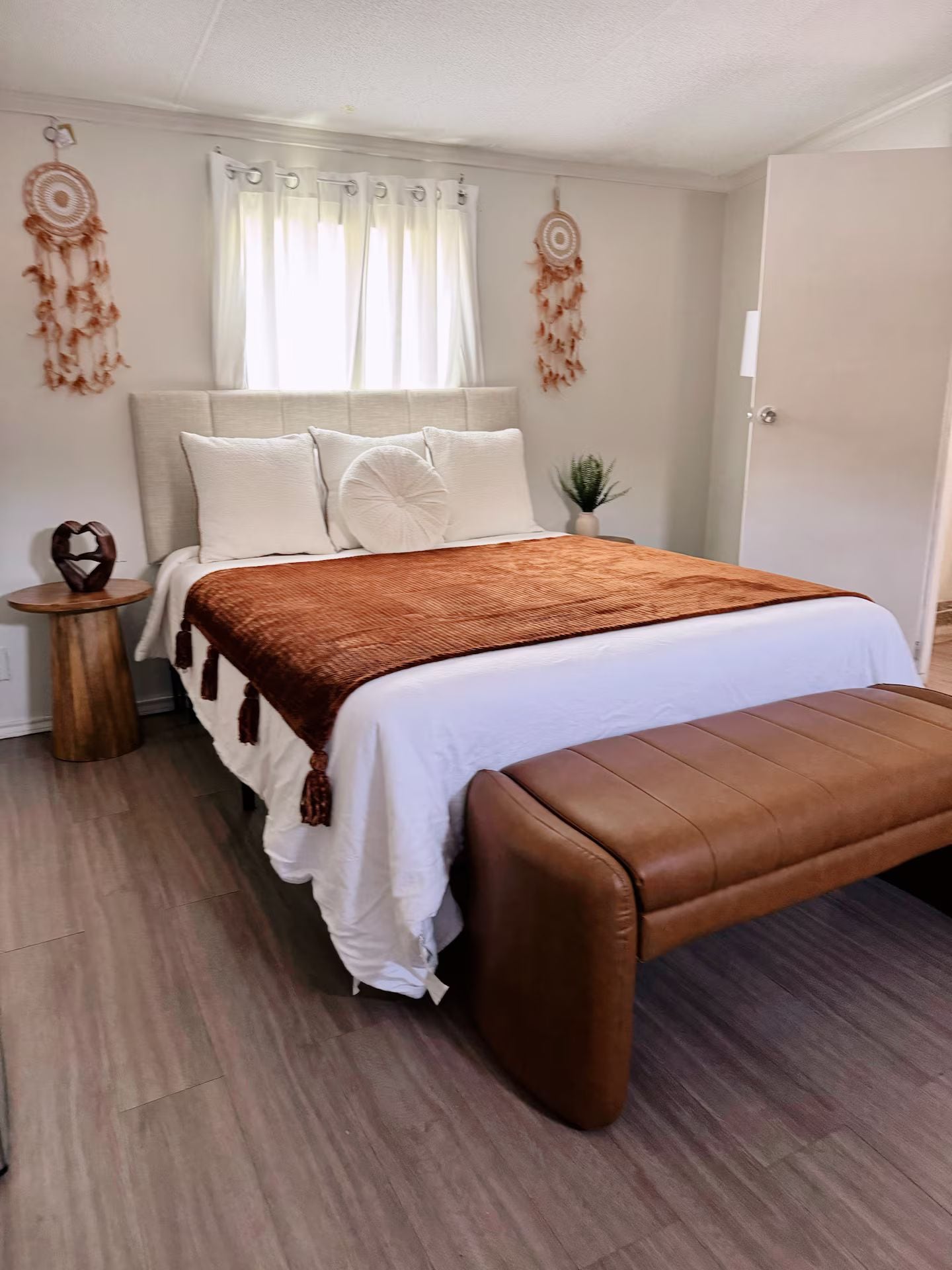 Quarto com cama, almofadas, um banco, uma mesa pequena e decorações nas paredes.