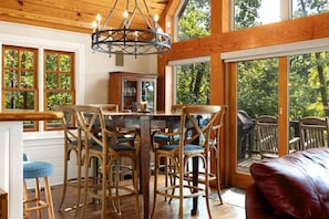 A wooden dining area with a chandelier, a glass cabinet, and a view of the outdoors. - Summer Place A-Frame • Luxury Main Lake A-Frame • Private Beach + Sleeps 10 (Littleton)