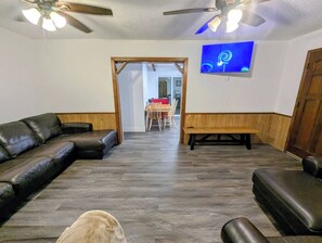 Une pièce comprenant un canapé d’angle, un banc, un ventilateur de plafond et un téléviseur fixé au mur.