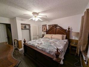 A bedroom with a wooden bed, a ceiling fan, a bedside table, and a nightstand. - Dog Friendly • Porch Escape • 7 Miles to Beach (Gulfport)