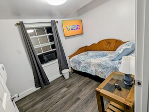 A bedroom with a bed, a bedside table with a lamp, a window with curtains, and a wall-mounted TV displaying 'VIZIO'. - Dog Friendly • Porch Escape • 7 Miles to Beach (Gulfport)
