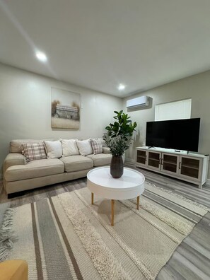 Ein Wohnzimmer mit einer Couch, einem runden Couchtisch mit einer Pflanze, einem Flachbildfernseher und einem Schrank.