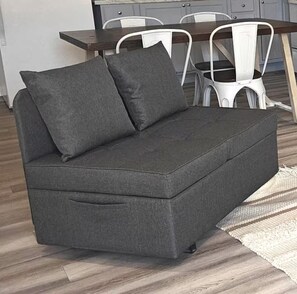 Ein graues Sofa mit Kissen, ein Esstisch mit Stühlen und ein gemustertes Teppich.