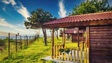 A wooden cabin with a tiled roof, a fenced garden, and a view of the sea.