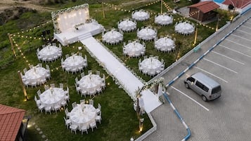 Un lugar para bodas al aire libre con mesas redondas, un escenario y una cancha de baloncesto.
