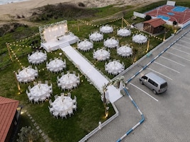 Un lugar para bodas al aire libre con mesas redondas, un escenario y una cancha de baloncesto.