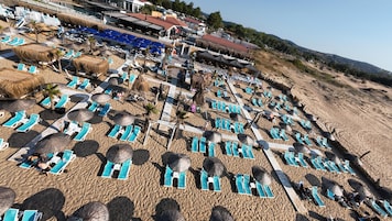 Una playa con filas de tumbonas y sombrillas, un muelle de madera y vistas del pueblo al fondo.