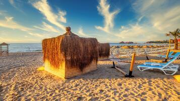 A beach with a thatched hut, sun loungers, and umbrellas.