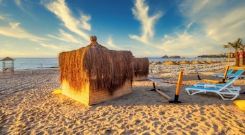 Una playa con una cabaña de techo de paja, tumbonas y sombrillas.