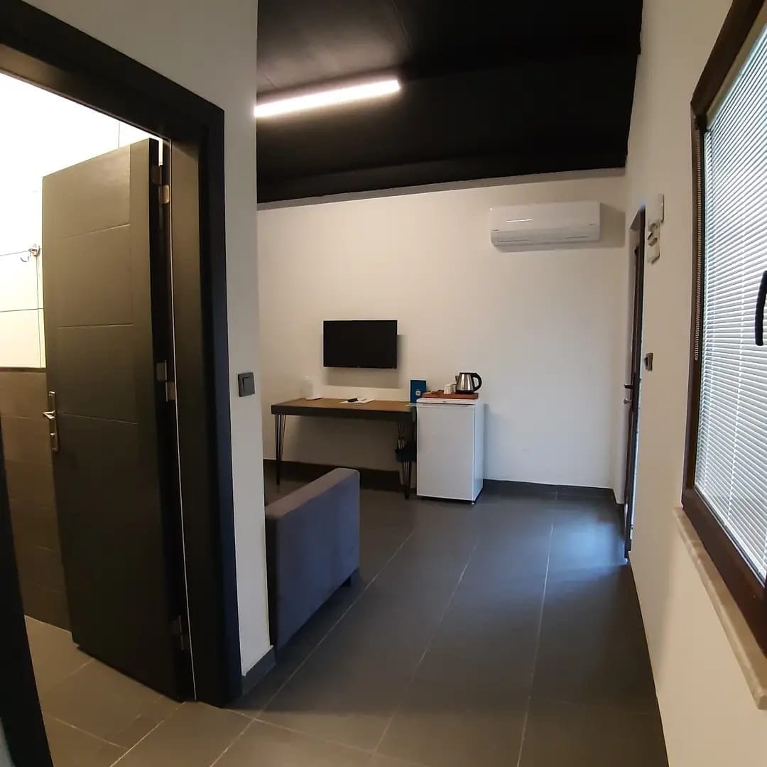 A hallway with a door, a desk with a computer, a small refrigerator, and an air conditioning unit.
