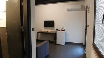 A hallway with a door, a desk with a computer, a small refrigerator, and an air conditioning unit.