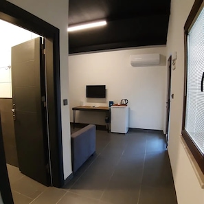 Un pasillo con una puerta, un escritorio con una computadora, un refrigerador pequeño y un equipo de aire acondicionado.