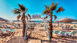 Een strand met ligbedden, palmbomen en een bord met de tekst 'Marin Beach Hotel'.