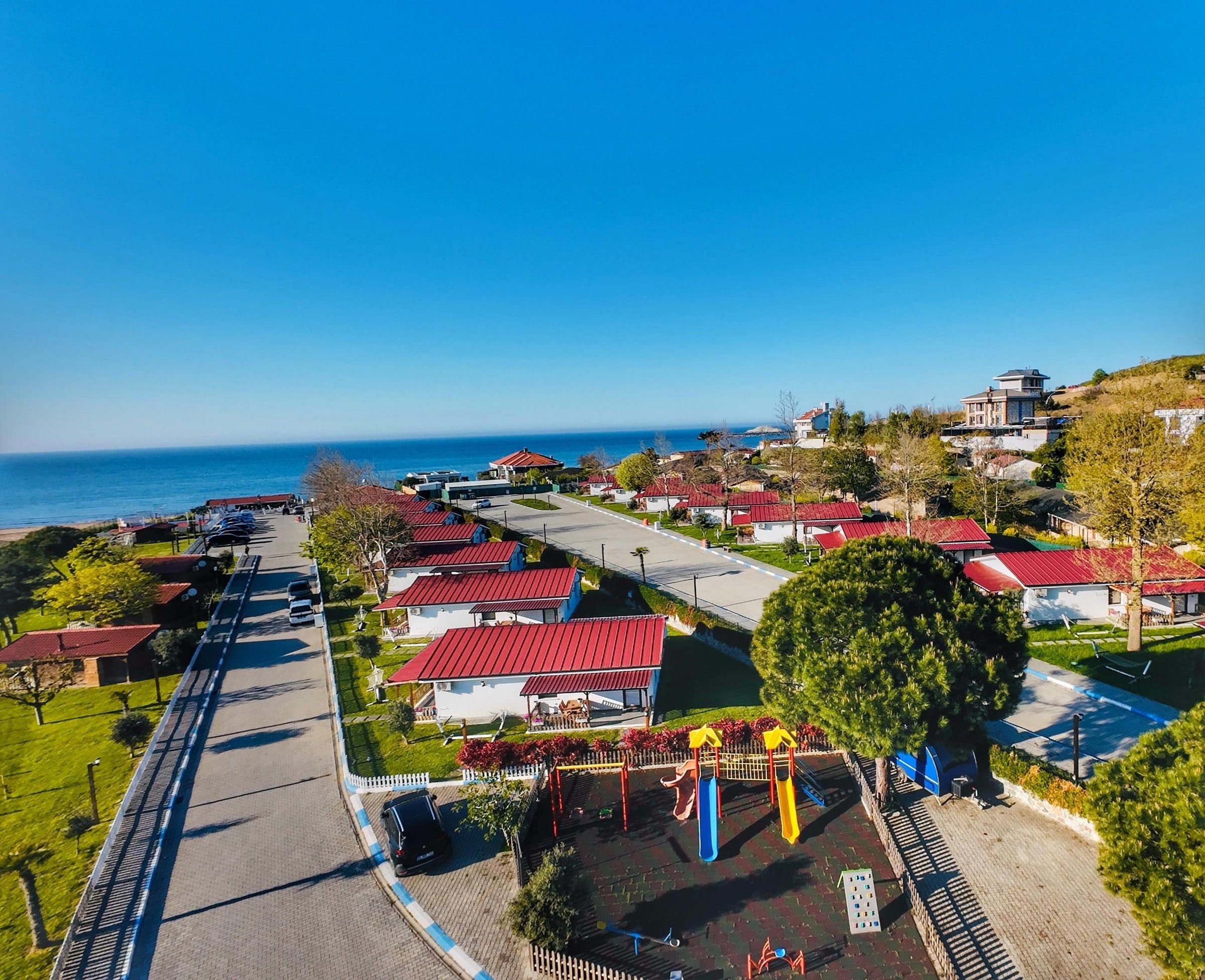 Zona residencial costera con casas, un parque infantil y una vista despejada del mar.