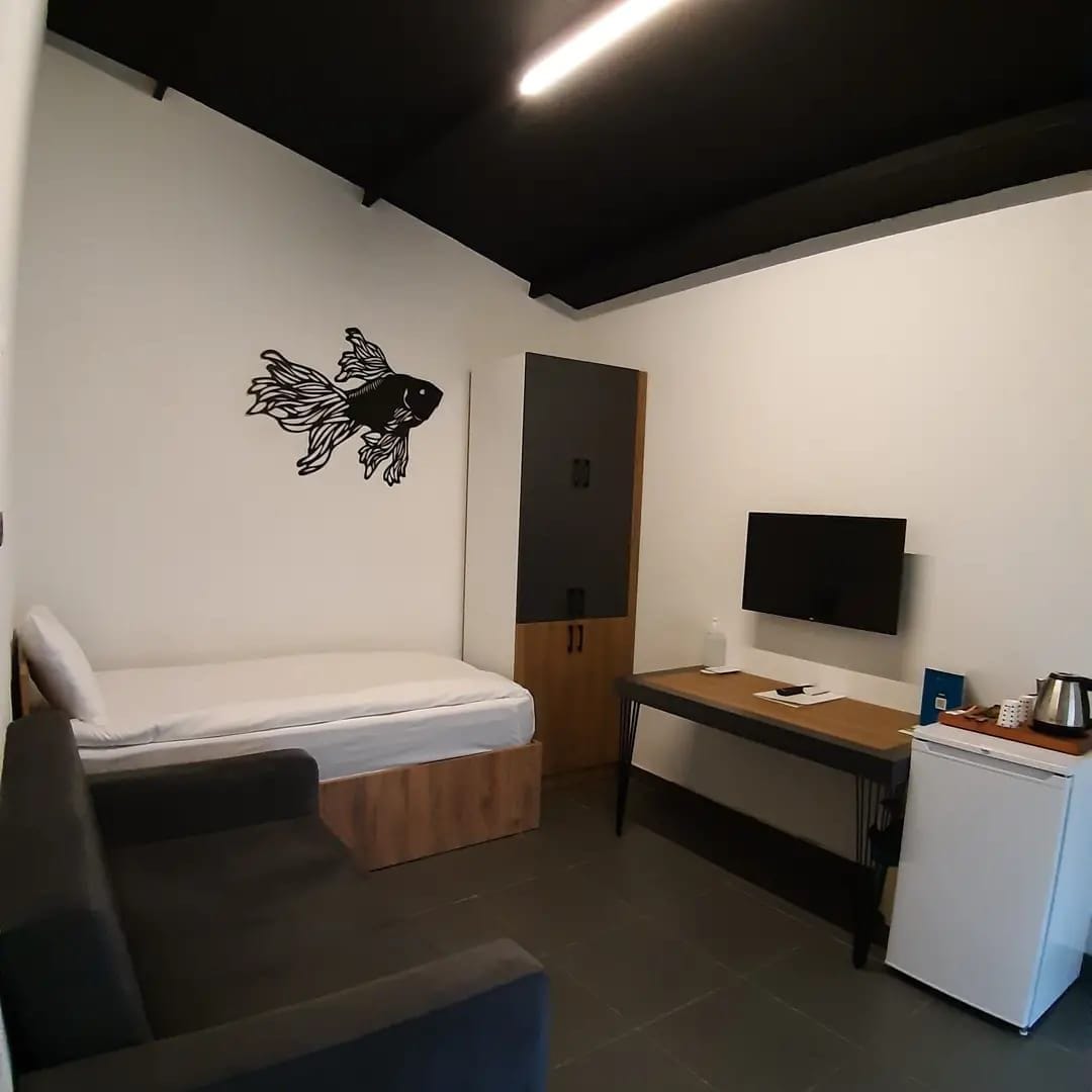 Una habitación compacta con cama, escritorio, televisor y un refrigerador pequeño.