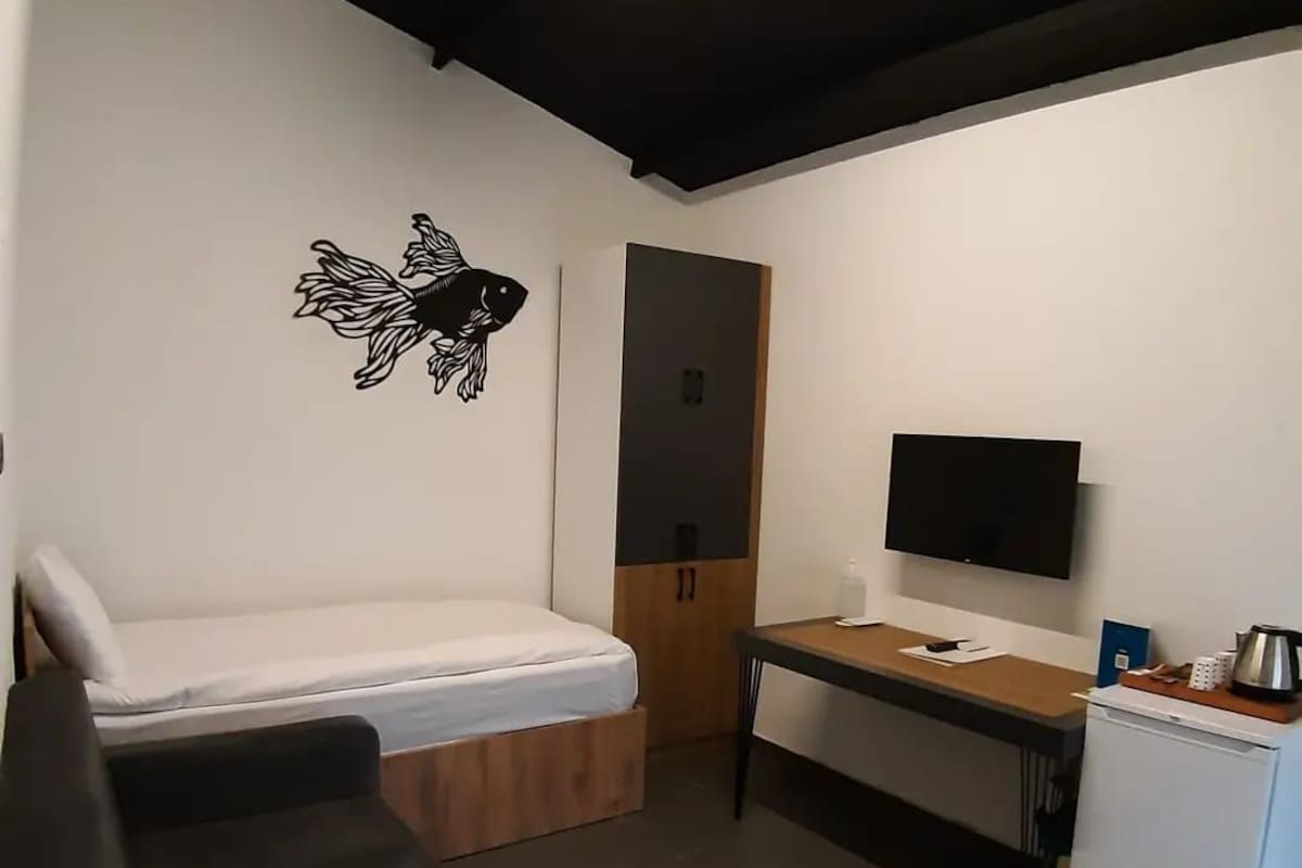 Een kleine kamer met een bed, een bureau, een televisie en een kleine koelkast.
