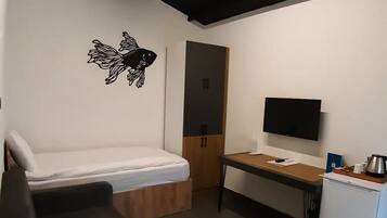 A compact room with a bed, a desk, a television, and a small refrigerator.