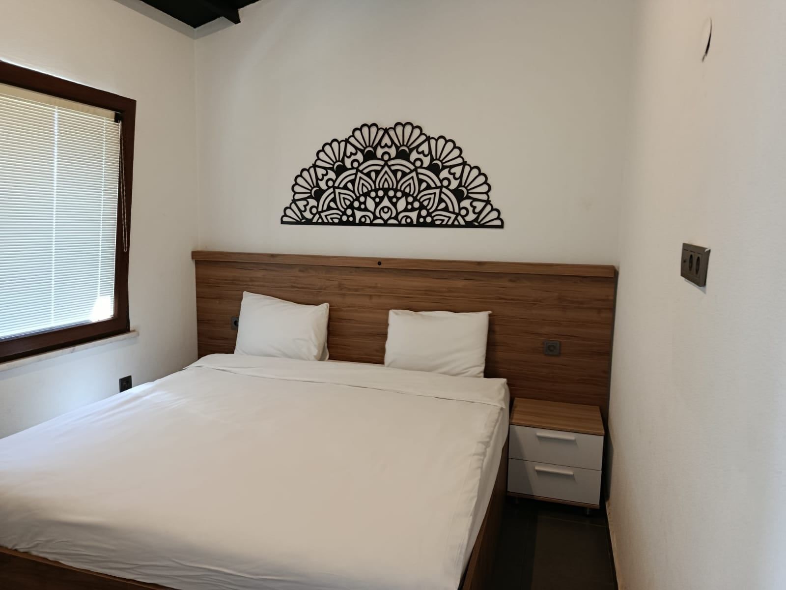 Un dormitorio con cabecera de madera, cama con ropa de cama blanca, mesita de noche y un adorno en la pared.