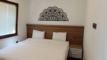 Un dormitorio con cabecera de madera, cama con ropa de cama blanca, mesita de noche y un adorno en la pared.