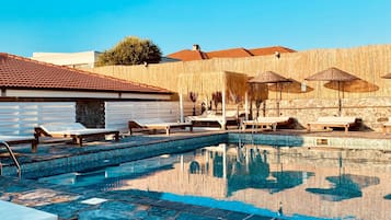 A swimming pool with lounge chairs and umbrellas, surrounded by a wooden fence and buildings.