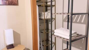 Habitación de hotel con literas, una mesita de noche pequeña con lámpara y un armario con estantes.