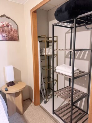 Habitación de hotel con literas, una mesita de noche pequeña con lámpara y un armario con estantes.