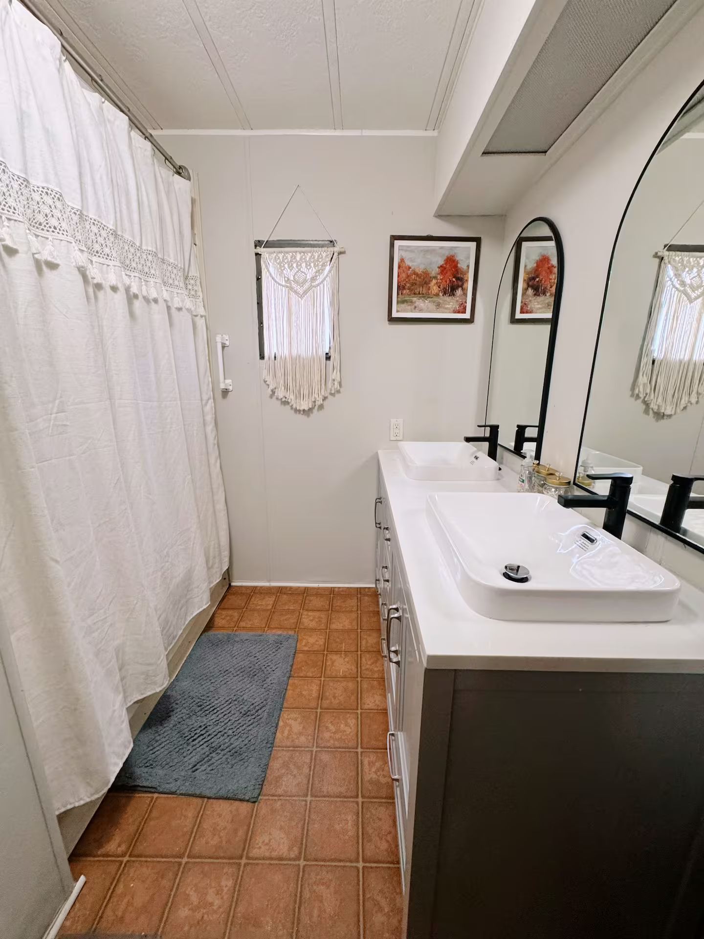 Casa de banho com lavatório branco, espelho, cortina de chuveiro e tapete pequeno.