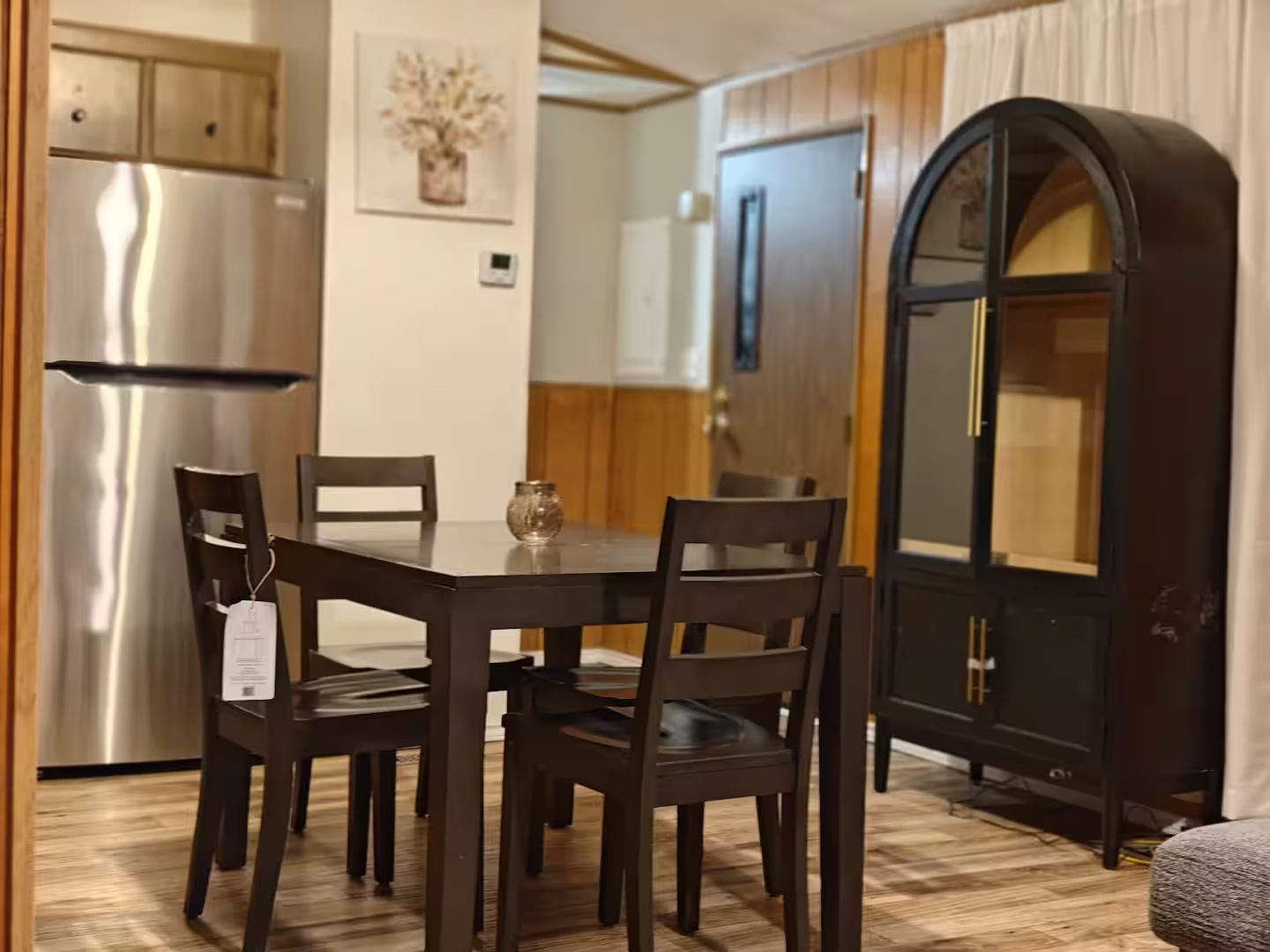 Un comedor con una mesa y sillas de madera, un refrigerador y un armario con un jarrón en la pared.