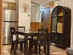 Un comedor con una mesa y sillas de madera, un refrigerador y un armario con un jarrón en la pared.