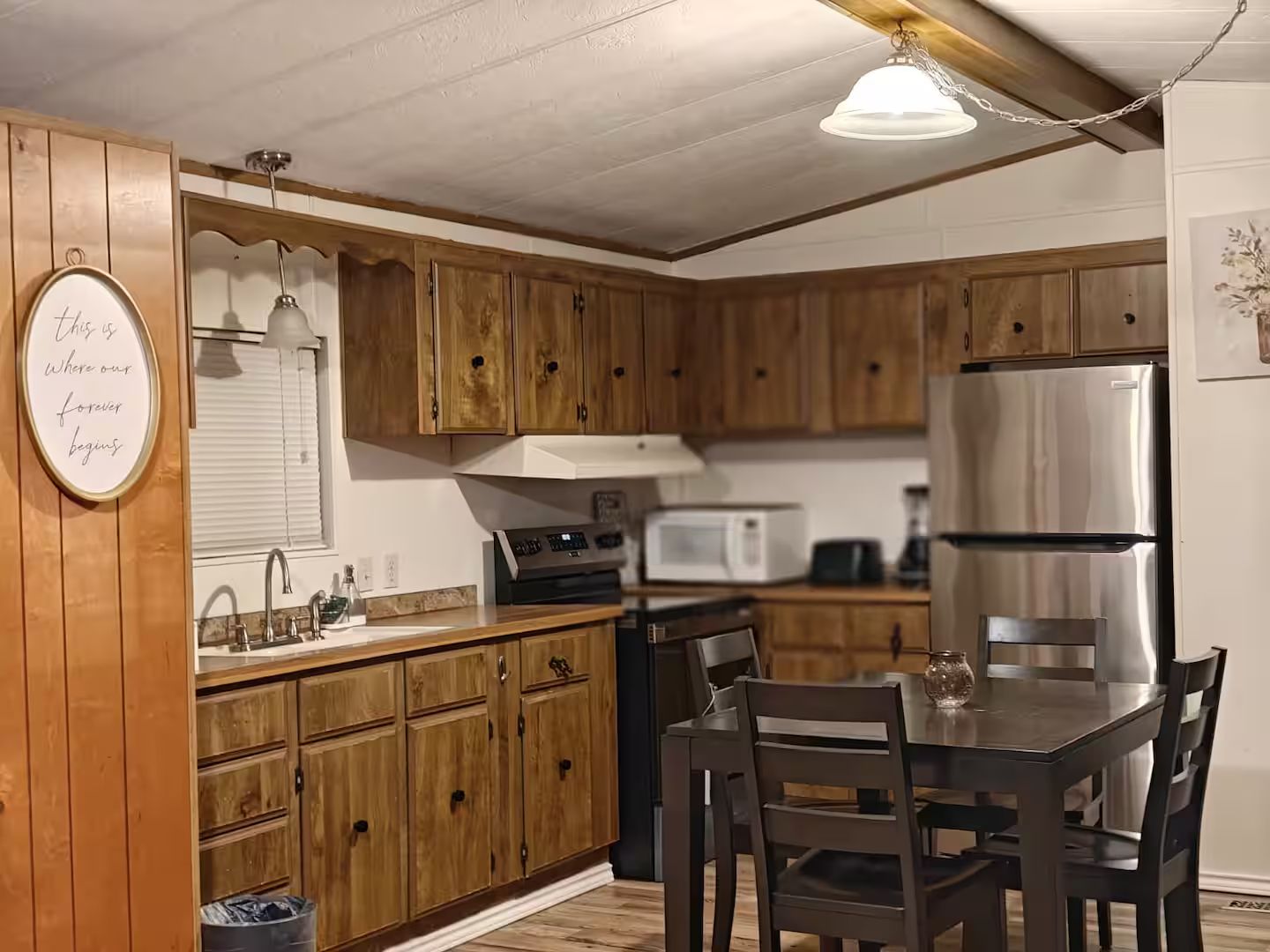 Une cuisine avec des meubles de rangement en bois, un réfrigérateur en acier inoxydable, un four à micro-ondes et une table à manger avec des chaises.