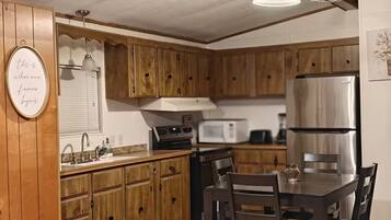 Une cuisine avec des meubles de rangement en bois, un réfrigérateur en acier inoxydable, un four à micro-ondes et une table à manger avec des chaises.
