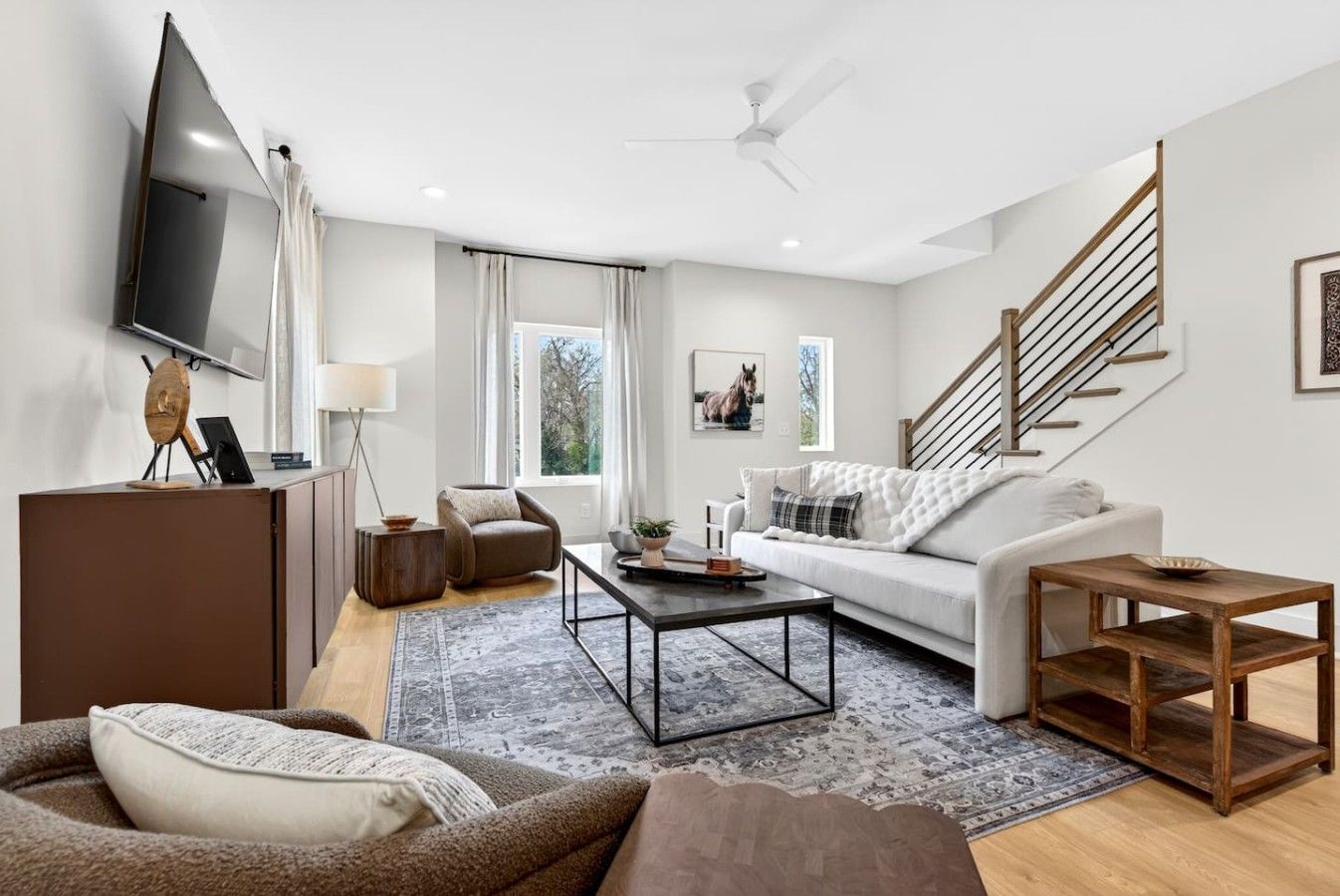 A modern living room with a flat-screen TV, a sofa, a coffee table, and a staircase.