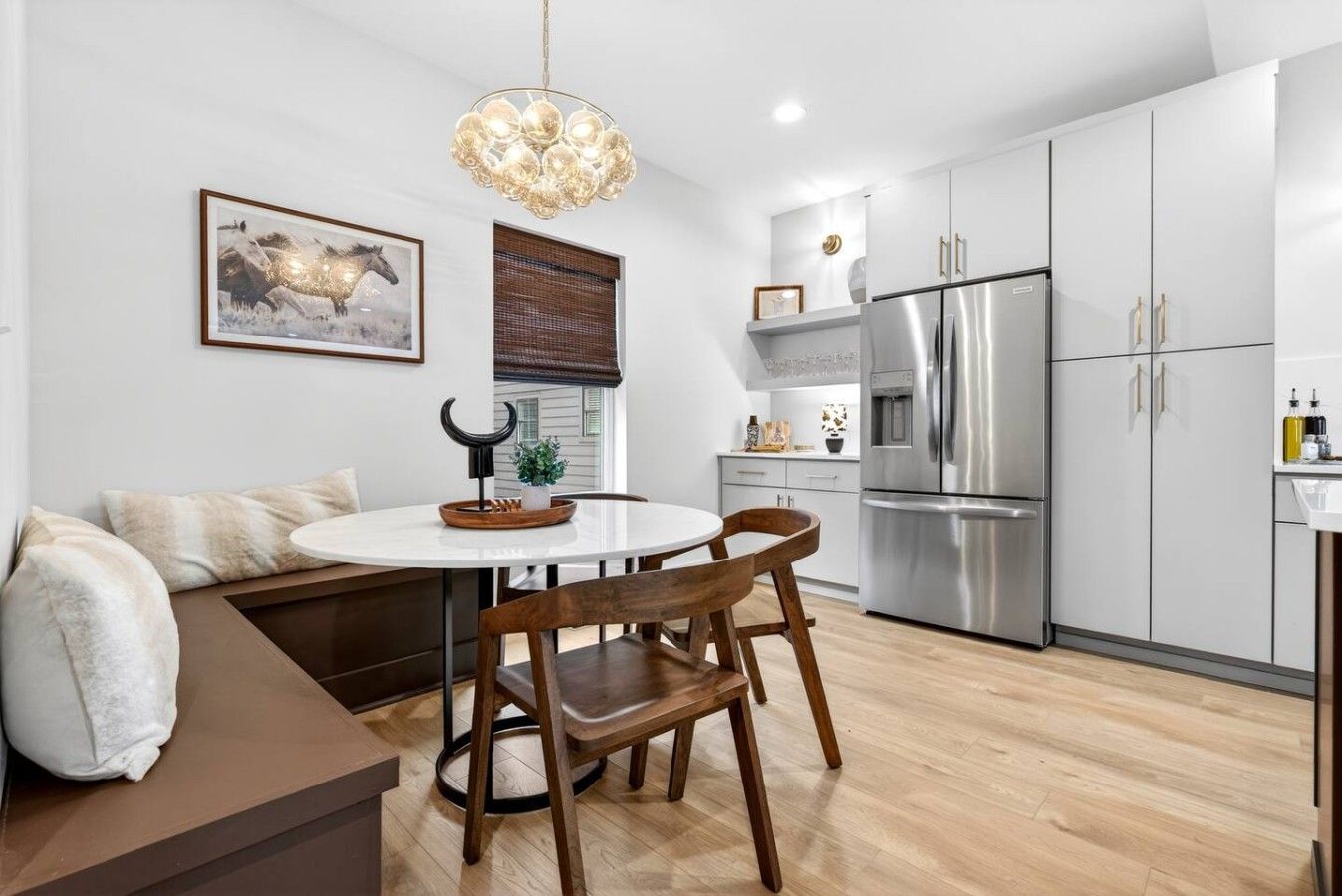 A modern kitchen with a stainless steel refrigerator, wooden chairs, a round table, and a hanging light fixture.