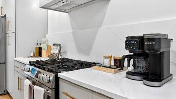 A modern kitchen with a gas stove, a coffee maker, and a marble countertop.