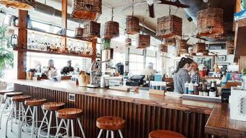 Un bar doté de nombreux tabourets, d’un comptoir avec les ustensiles nécessaires et de paniers suspendus.