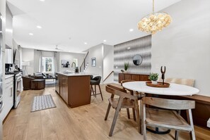 A modern kitchen with a central island, a dining area with a round table and wooden chairs, and a staircase leading to an upper level. - Home with Garage, Rooftop with BBQ Grill & TV, 3 Miles to Downtown (Nashville)