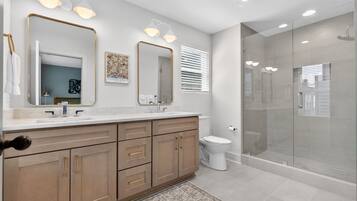 Un baño moderno con tocador doble, cabina de ducha con mampara de vidrio y retrete.