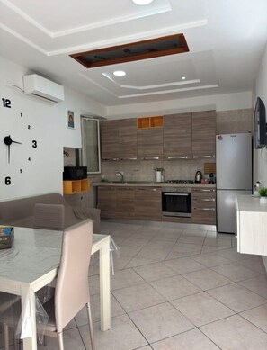 A modern kitchen with a dining area, featuring a clock, cabinets, and a refrigerator. - Frankie’s House – La tua casa a Napoli (Napoli)