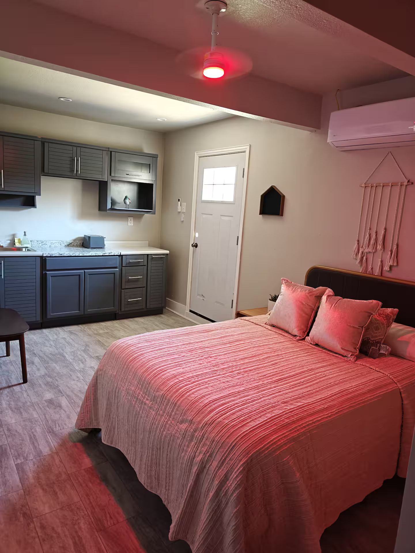 A bedroom with a large bed, a nightstand, a dresser, and a kitchen area with cabinets and a countertop.