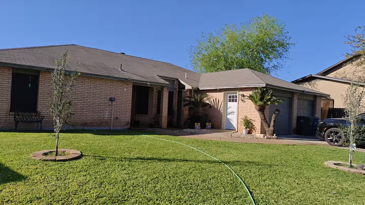 A residential house with a brick exterior, a front door, a garage, and a well-maintained lawn.